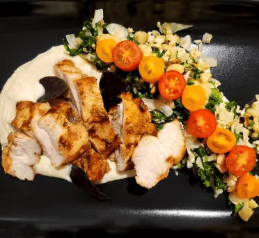 A plate of grilled chicken with cherry tomatoes and greens